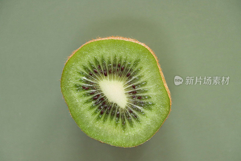 猕猴桃/中国猕猴桃(Actinidia chinensis)的特写图片，切成两半，显示模糊的棕色皮肤和亮绿色的果肉，黑色的种子环，绿色背景，高架视图